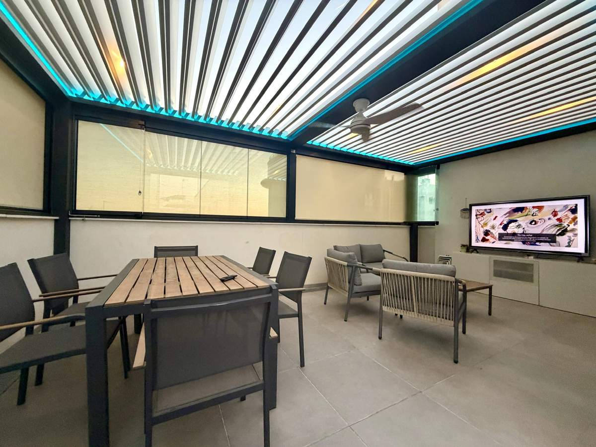 Ático cerrado con pérgola bioclimática, cortinas de cristal e iluminación LED en tono azul