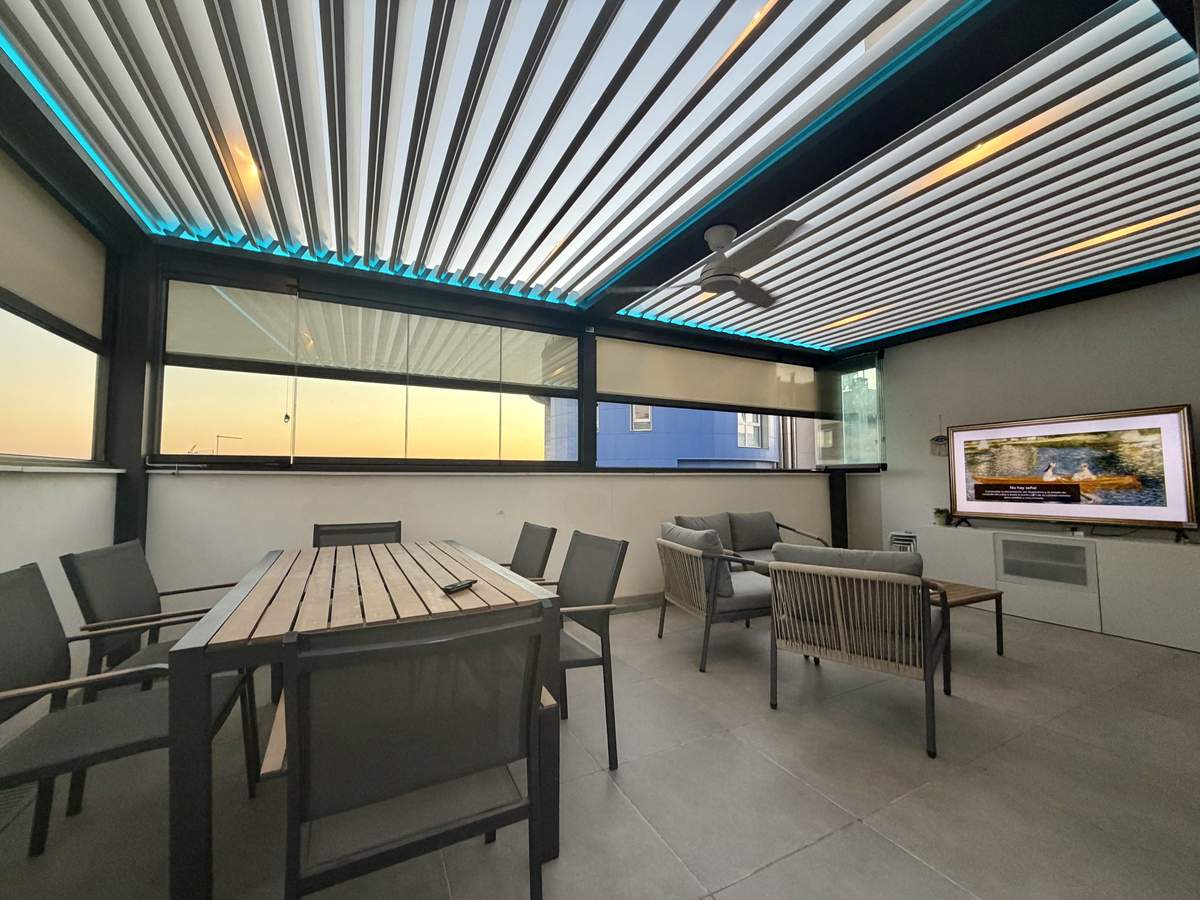Comedor y zona de estar bajo la pérgola bioclimática iluminada